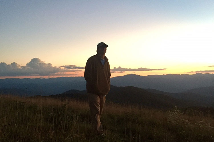 man walking on hilltop at sunset