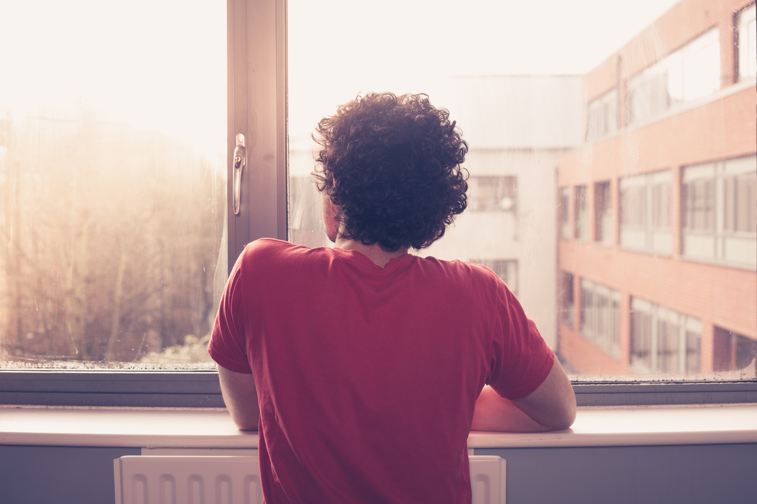 man staring into sunrise out of window