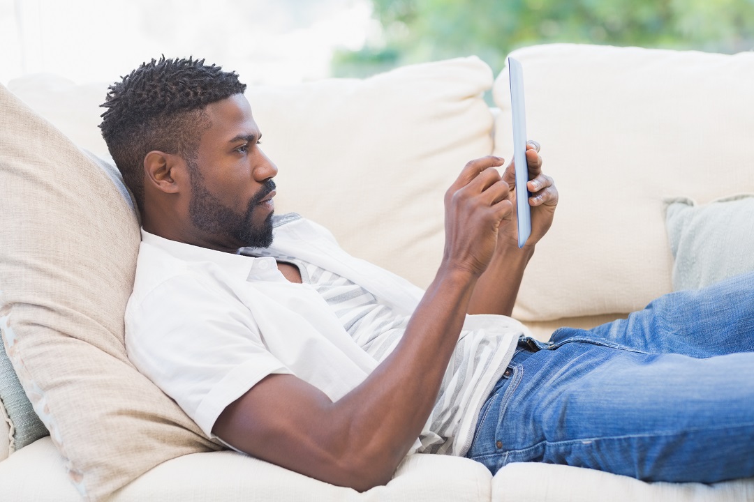 man on couch reading from tablet