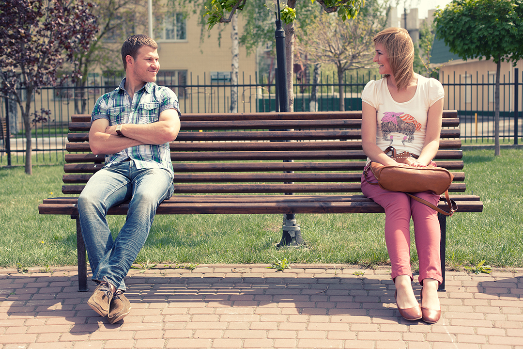man and woman smiling at each other while sitting on bench