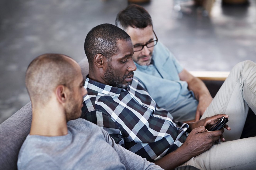 three men look at phone while sitting on a couch