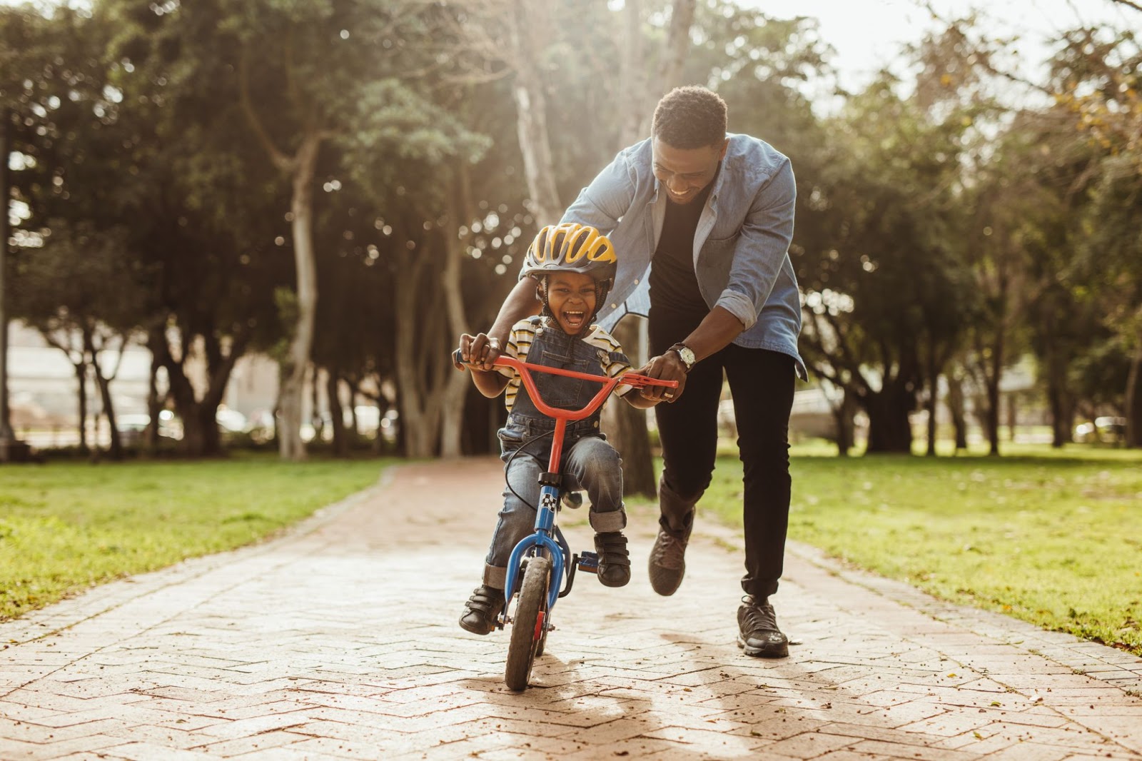 African American dad teaching his son how to ride a bike in the park