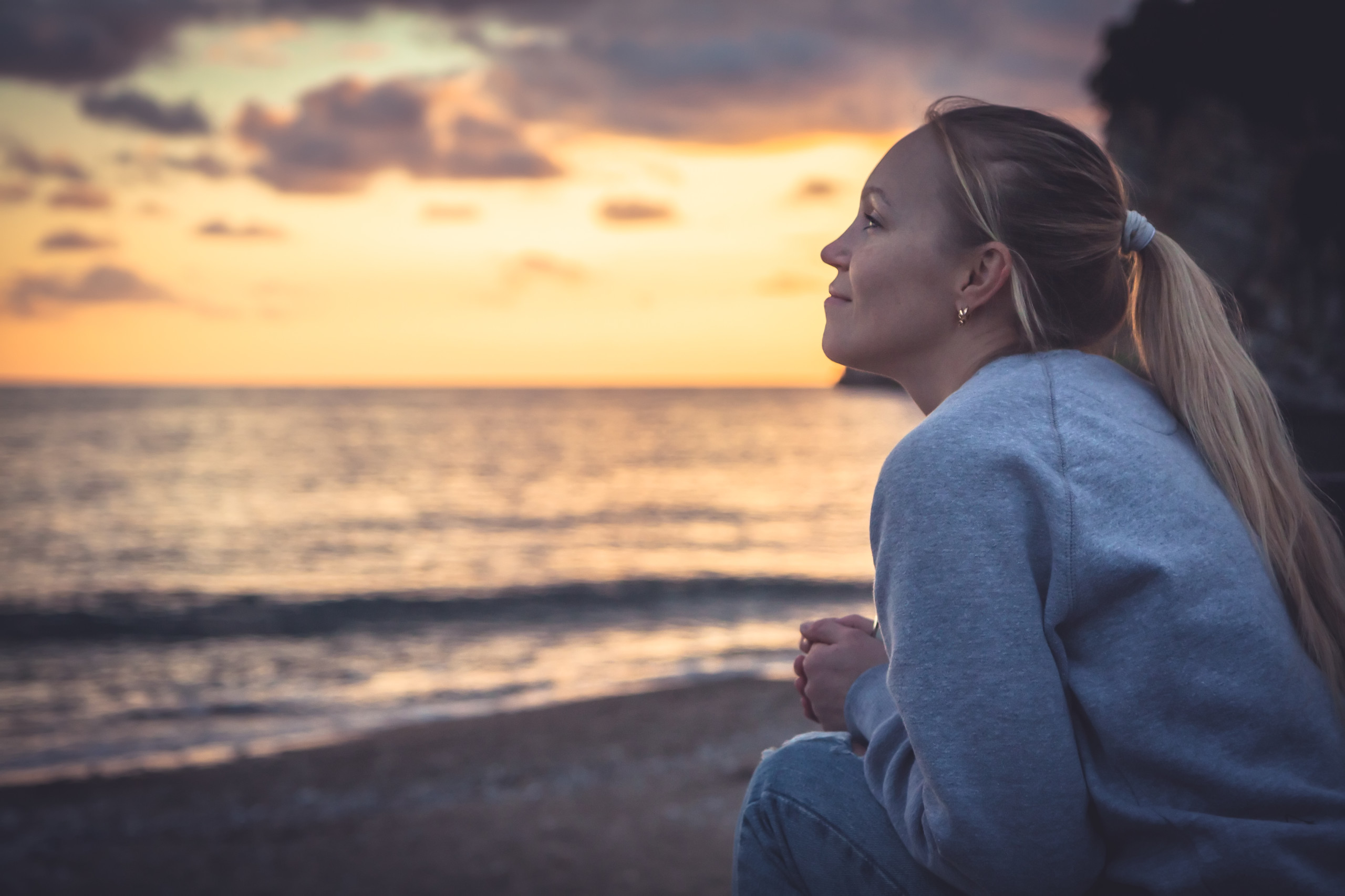 Pensive lonely smiling young woman looking with hope into horizon during sunset at beach