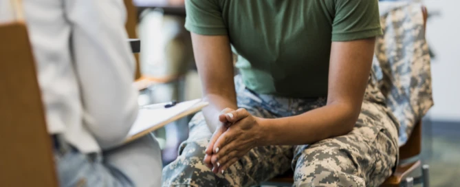 A close up photo of an unrecognizable mid adult female soldier as she puts her hands together and leans forward in her seat.  She is talking with an unrecognizable female counselor.