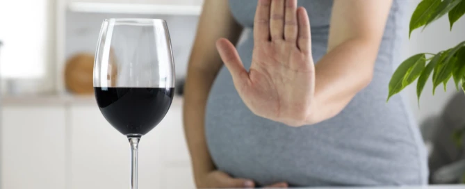 Pregnant woman show NO gesture to glass of wine. Pregnancy and alcohol. Prenatal care and unhealthy lifestyle.